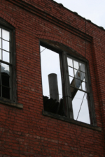 The factory's old smokestack seen through a busted window.