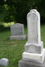 The tombstone of the wife of Henry Newman in the foreground with the marker for Robert and Julia Fuller in the background.