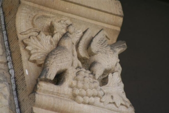 A couple of birds eating grapes was engraved next to a window.