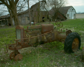 One of the two old rusted tractors in the backyard of the house.